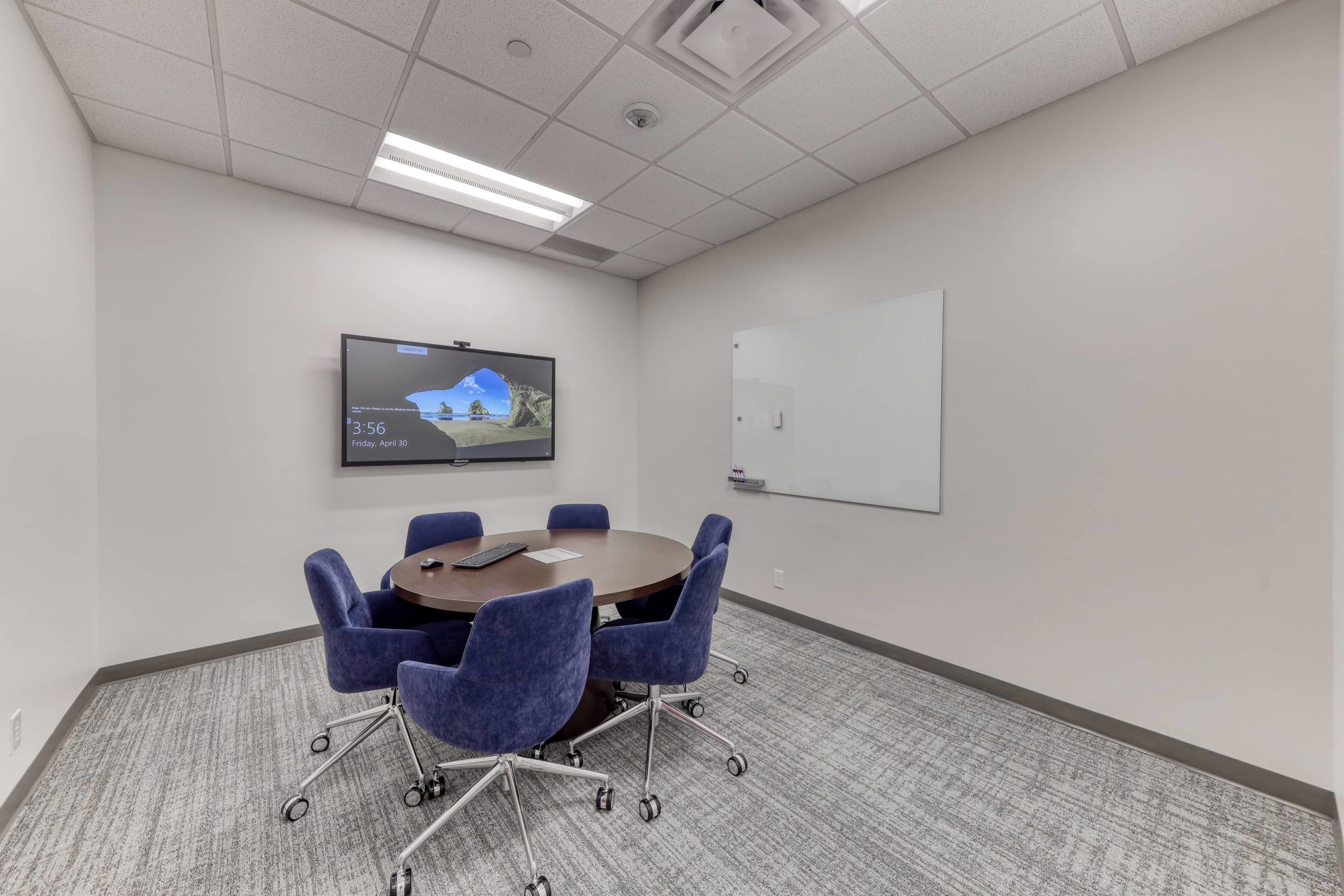 Small meeting room with round table, rolling chairs, wall-mounted display, and whiteboard for team collaboration.