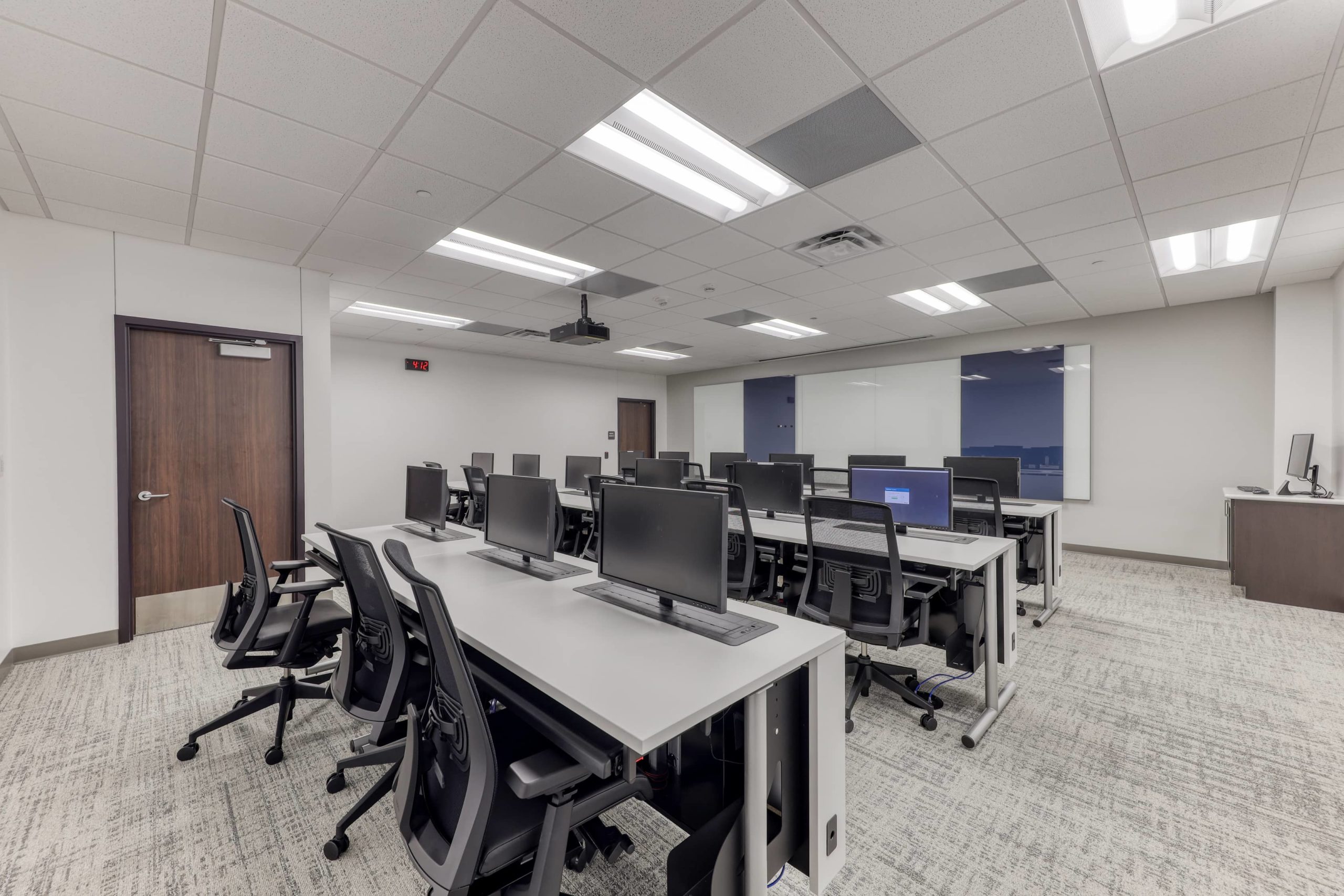 Computer training classroom with desktop workstations, rolling task chairs, instructor podium, and projection equipment.