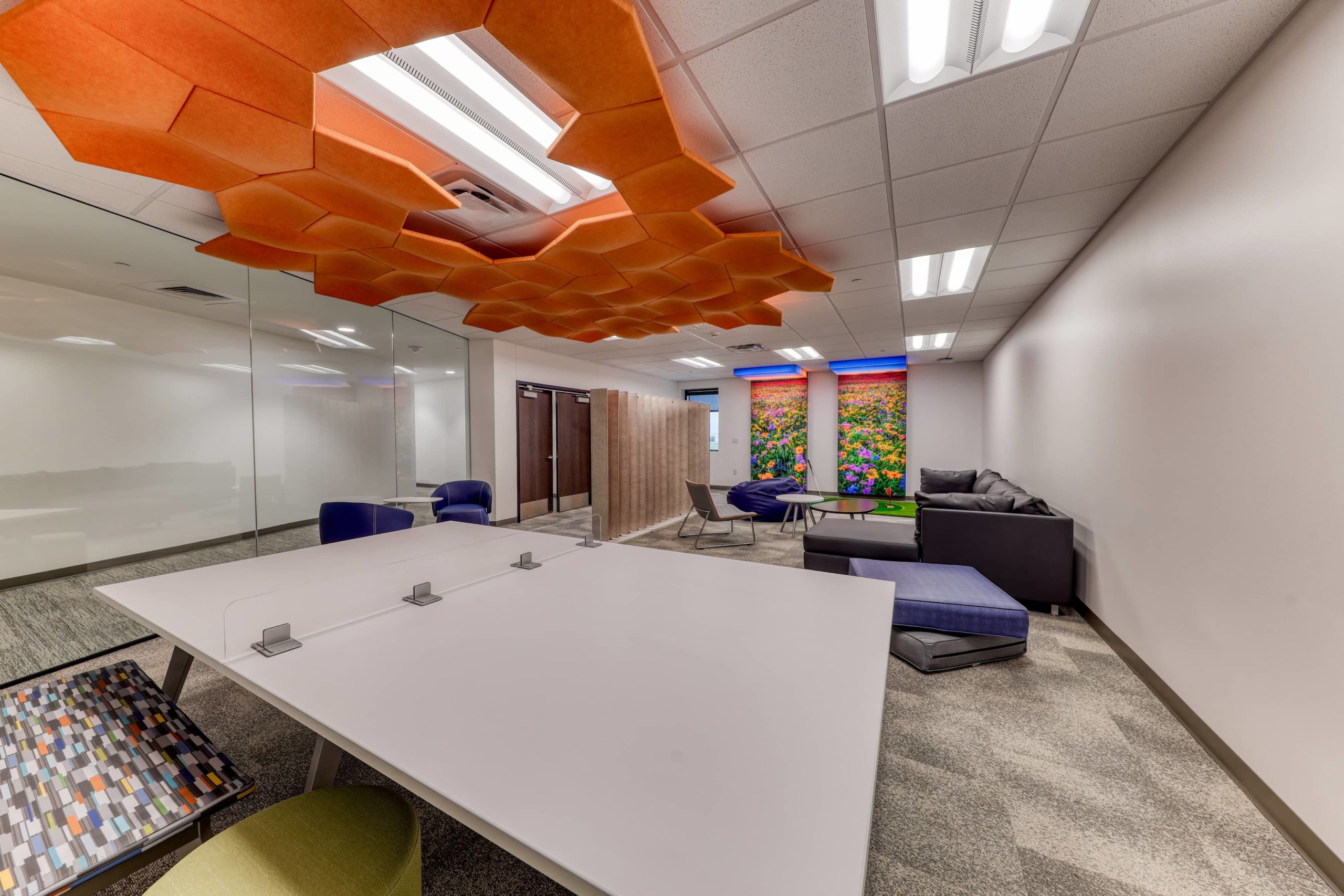 Flexible collaboration space with large worktables, lounge seating, ceiling-mounted acoustic panels, and movable dividers.