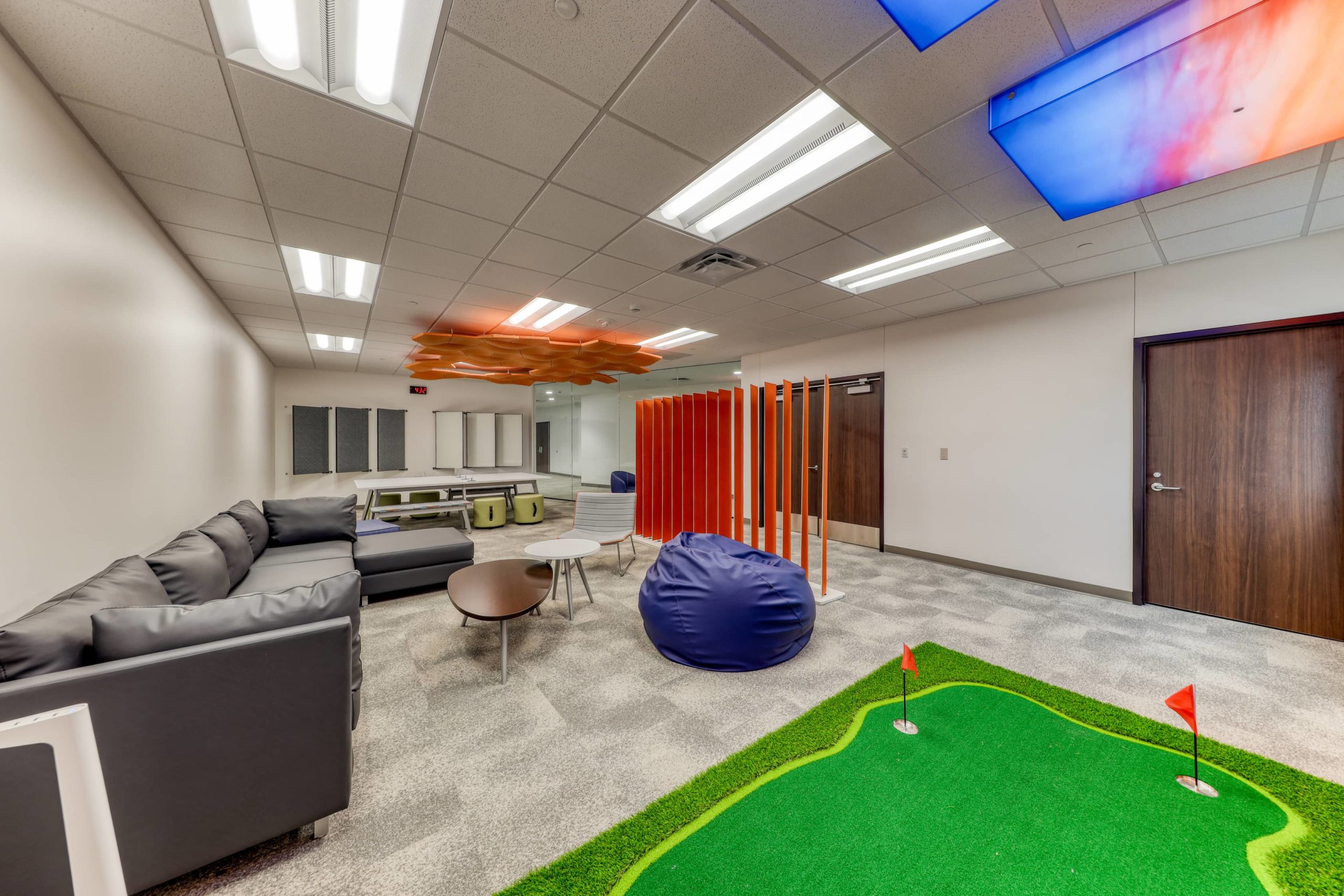 Open lounge area featuring sofas, beanbag seating, divider panels, and a small putting green for informal engagement.