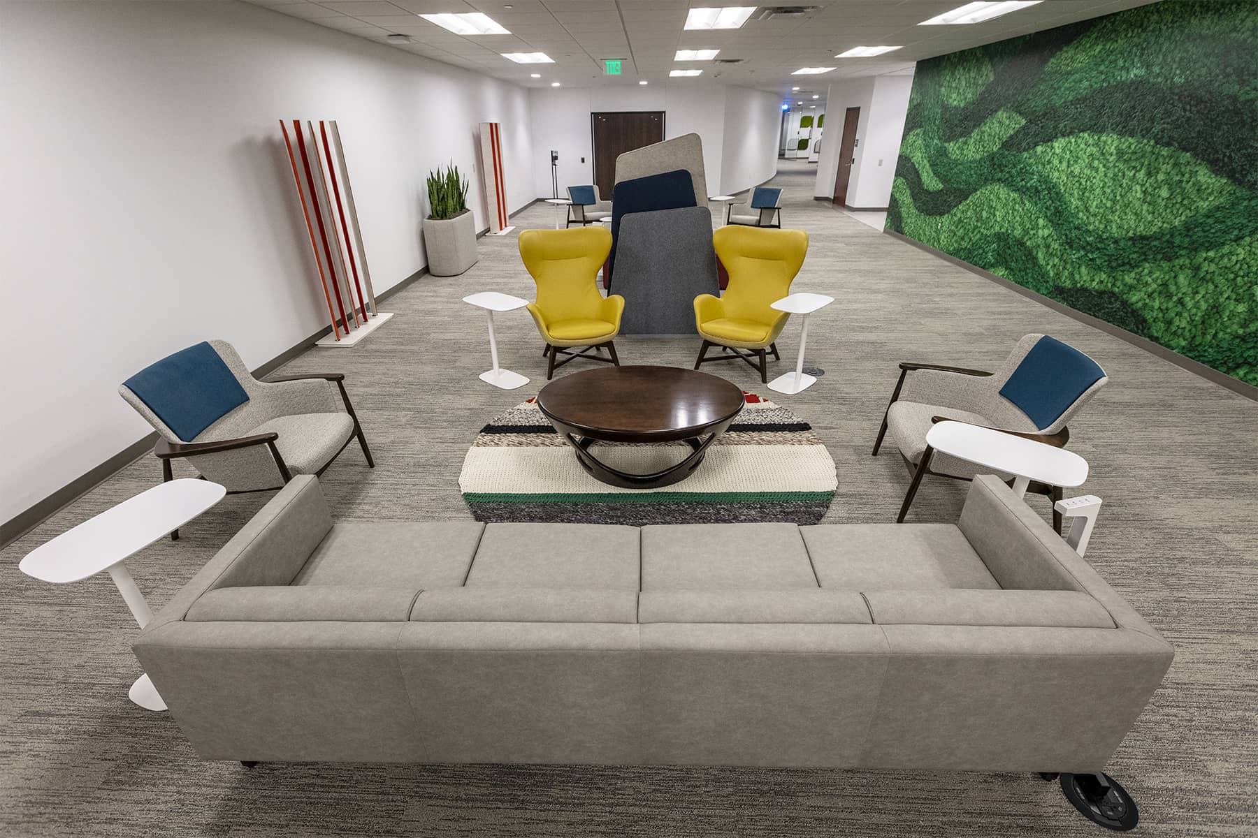 Modern lounge area with sofas, accent chairs, small tables, and movable privacy panels for informal meetings and breakout discussions.