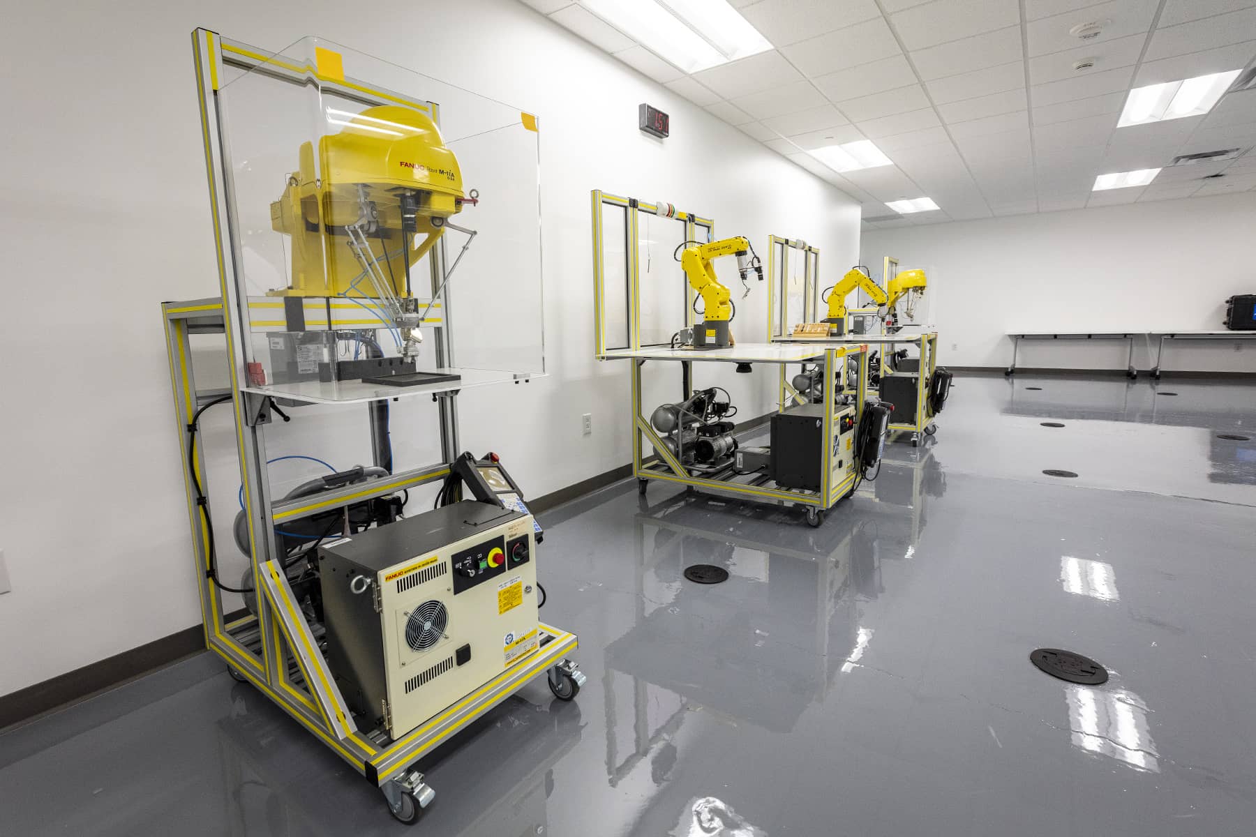 Technical training lab with industrial equipment and robotic training stations arranged along a polished floor workspace.