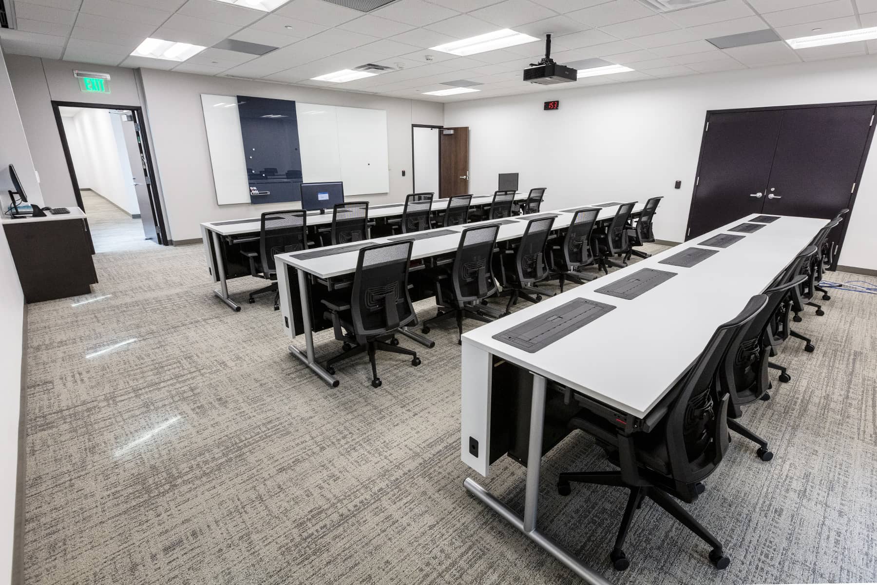Classroom-style training room with rows of tables, rolling chairs, instructor station, and wall-mounted presentation displays.