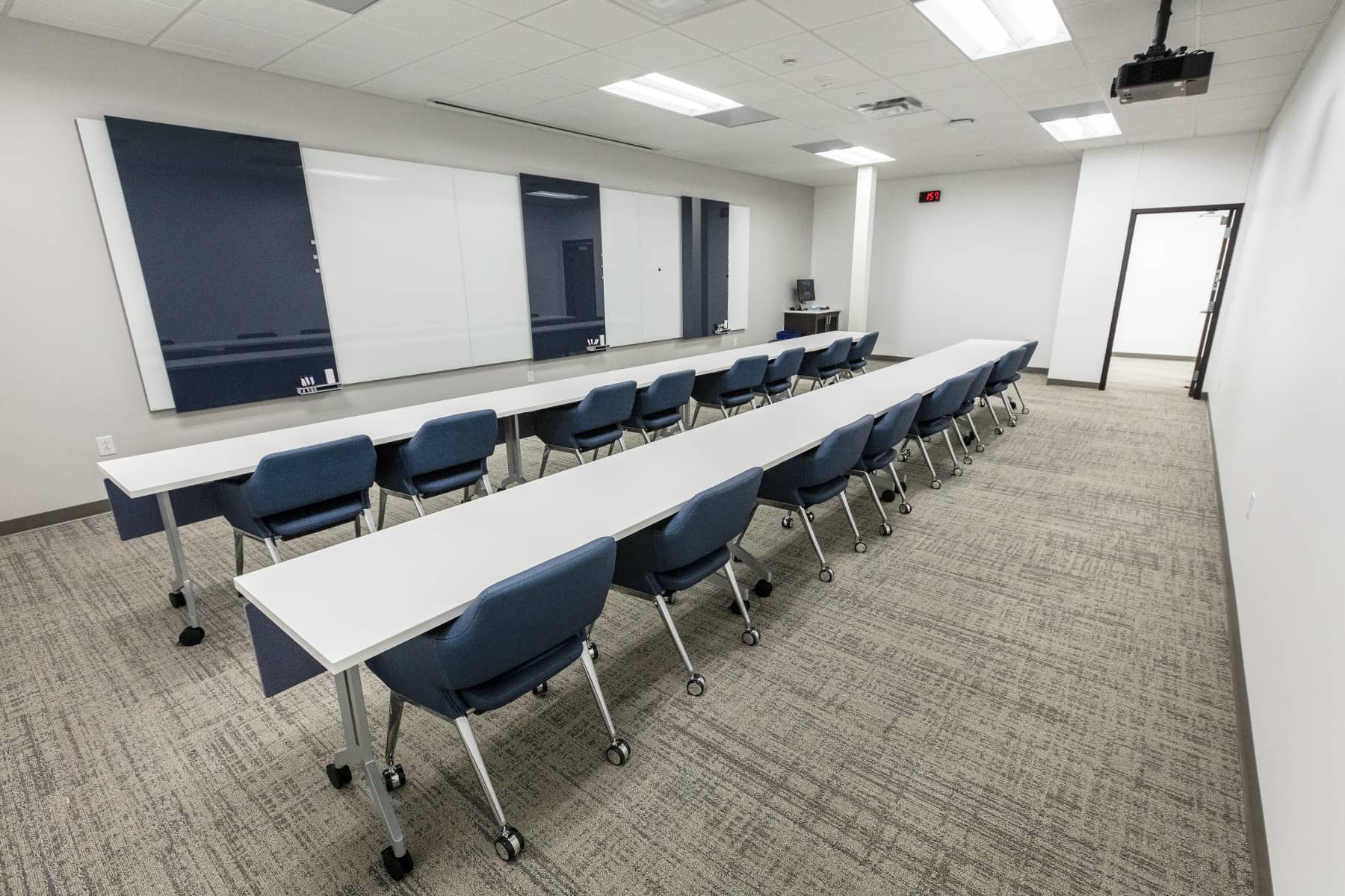 Long training room with modular tables, mobile chairs, and large writable wall panels for instruction and group work.