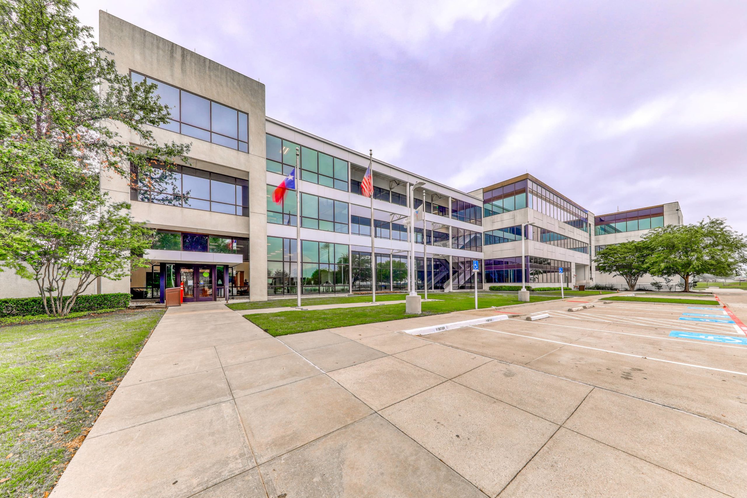 Exterior view of a modern office and training facility building with glass facade, flagpoles, and parking area.