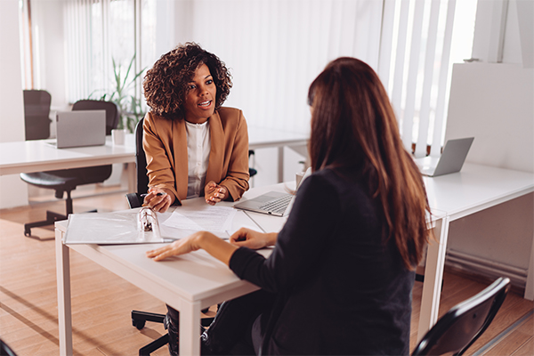 A woman receives advice from another woman seated across from her at a desk